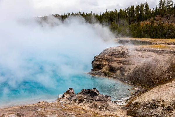 Natural scene of boilng blue pond geyser basin with white smoke inside dangerous hot zone in Yellowstone national park, Wyoming, USA.