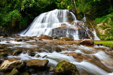 Yağmur mevsiminde tropikal yağmur ormanlarının içindeki kayalık şelaleden akan suyun uzun pozlu fotoğraf tekniği..
