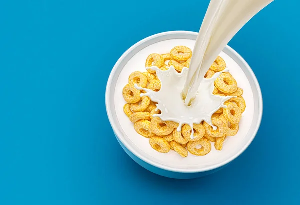 牛乳を注ぎ 青い背景にスプラッシュとコーンリングの朝食のボウル トップビュー — ストック写真
