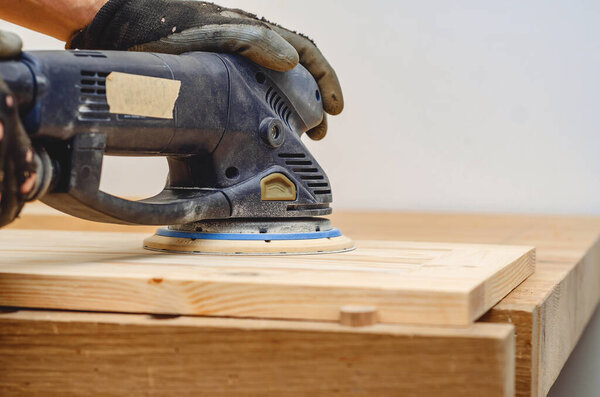 Joiner's tools. Sanding a wooden board with a hand-held electric sander