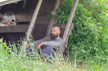 Viking savaşçısı savaştan sonra tahta binanın yakınında dinleniyor. Metal zincir zırh ve kask. Yeşil çalılar.