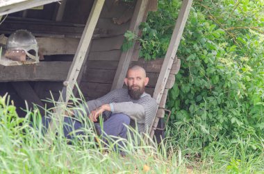 Viking savaşçısı savaştan sonra tahta binanın yakınında dinleniyor. Metal zincir zırh ve kask. Yeşil çalılar.
