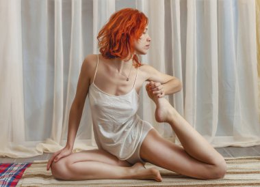 Esnek, genç ve güzel bir kadın spor yapıyor. Çıplak bacaklar ve omuzlar. Kızıl saçlı. Yan görüş. Evde sabahları esneme hareketleri. Sağlıklı yaşam tarzı. Evde kal konsepti