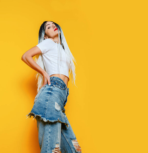 Bright photo of young woman on yellow background. Dreadlocks. White T-shirt and ripped jeans.