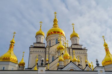 Bulutlu gökyüzüne karşı Ortodoks Hıristiyan dini binasının haçlı altın kubbeleri. Pochaiv. Ukrayna, 2022