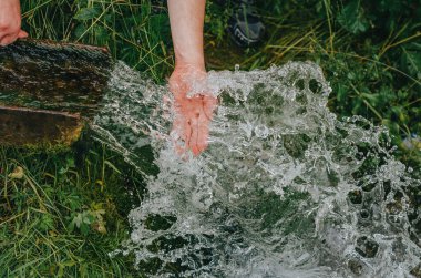 Sıcak yaz gününde soğuk temiz suyla serinlemek. Kaynağından temiz su akışı. Sudaki insan elleri.