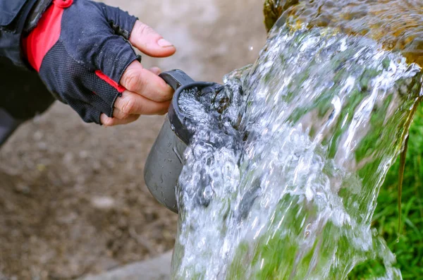 Sıcak yaz gününde soğuk temiz suyla serinlemek. Kaynağından temiz su akışı. Suda bir kupayla insan eli..