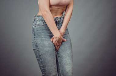 Kot pantolonlu ince kadın figürü. Eller bacak arasında. Aç karnına. Regl döneminde kadınların ağrısı.