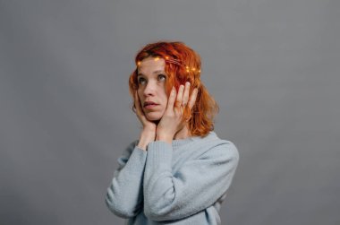 Kızıl saçlı, zarif, gizemli bir kadın. Işıklar saçta. Şaşırtıcı bir bakış. Gri arka plan. Yan görünüm.