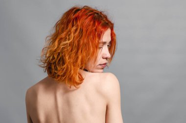 Sırtı çıplak, seksi genç bir kadın. Kızıl saçlı. Gri arkaplan
