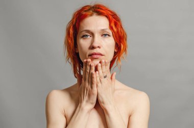 Kızıl saçlı çıplak kadın. Eller yüze yakın. Mavi gözler. Gri arkaplan