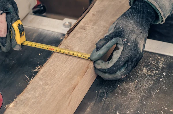 Marangoz ahşap tahtanın genişliğini mezura ile ölçer. Eldivenli marangoz elleri.