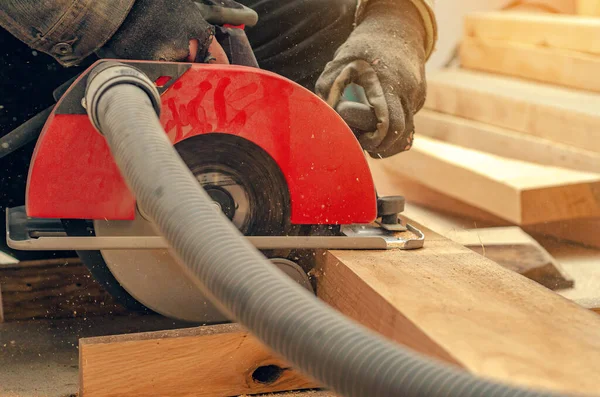 Cutting wooden board with electric saw in woodworking workshop. Joiner's hands. Close-up view.