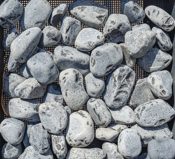 Round gray river stone. Lots of stones in construction sieve. Use of stones for treatment.