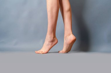 İnce kadın bacakları açık gri arka planda parmak uçlarında yükseliyor..