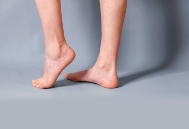Gri arka planda kadın uzun çıplak bacaklar. Ayaklar parmak uçlarında. Topuklu ayakkabılar. Güzellik salonu, tüy dökücü ilaç, varisli damar, estetik cerrahi, spa.