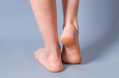 Gri arka planda kadın uzun çıplak bacaklar. Ayaklar parmak uçlarında. Topuklu ayakkabılar. Güzellik salonu, tüy dökücü ilaç, varisli damar, estetik cerrahi, spa.