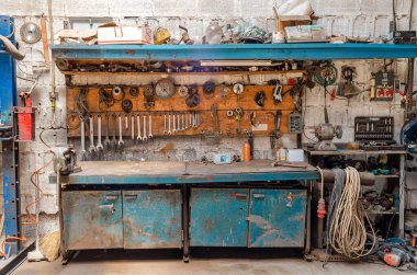 Masanın üstündeki duvarda çeşitli tamir aletlerinin eski bir koleksiyonu asılı. Aletli atölye.