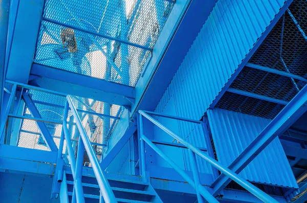 Construction grid. Iron blue stairs leading to production building. Modern solid stairs on background of plant.