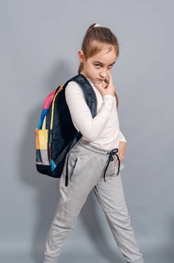 Sırt çantalı küçük kız. Sırt çantalı kız ciddi görünüyor ve kaşlarını çatıyor. Okulda sorunlar.
