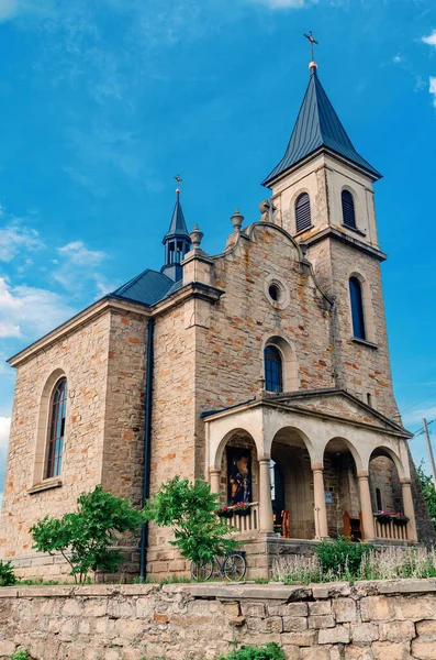 Catholic church on background of blue sky. Bicycle is parked near church.