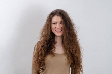 Cute girl is laughing and looking at  camera. Long curly dark hair, cute smile.