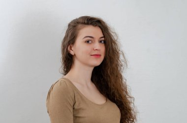 Photo of girl with long dark curly hair. Posing, thoughtful look. Side view. Gray background.