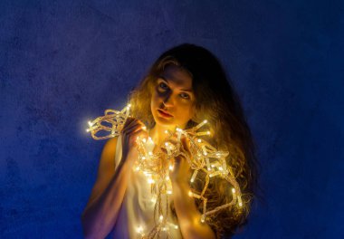 Atmospheric photo of young woman with garlands. Celebration concept. Romantic sexy picture with woman. Blue background.