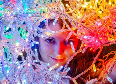 Face of  cute playful young woman through glow of bright colored lights. Fabulous winter photo.