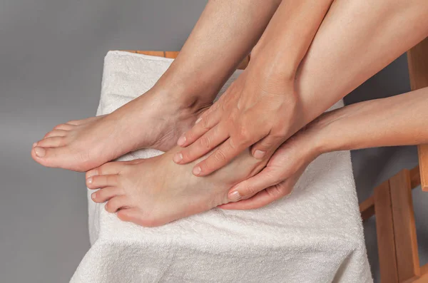 Female hands holding foot. Pain in  heel. Female feet on white towel.