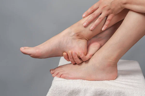 Female hands holding foot. Pain in  heel. Female feet on white towel.