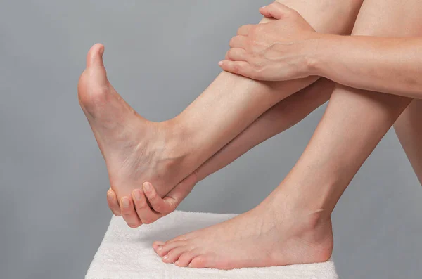 Female hands holding foot. Pain in  heel. Female feet on white towel. Heel massage.