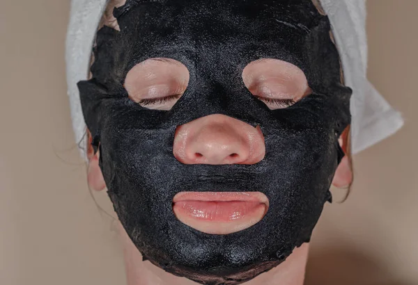 Black cosmetic fabric mask on woman\'s face. Face peeling mask with coal, spa procedures, skin care, cosmetology. Closed eyes.