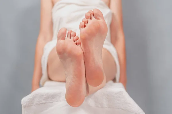 Female feet close-up. Sitting cross-legged. Blurred background of a female body in white towel.