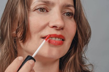 Woman paints her lips with red lipstick, close-up.