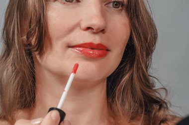woman paints her lips with red lipstick, close-up photo