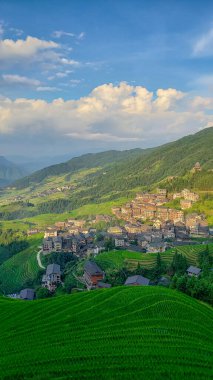 Bulutlu dağ manzarası. Yamaçlardaki evler. Çin. Dikey fotoğraf.