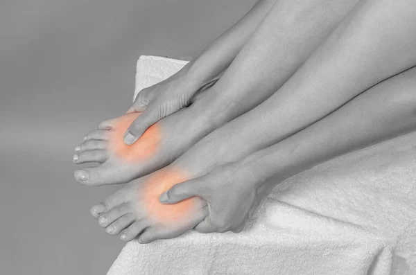 Point self-massage of feet. Woman touches her smooth legs, close-up. Legs and hands on white towel. Gray background.