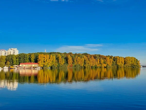 Blue lake in city. A forest on opposite bank of water. White clouds in sky