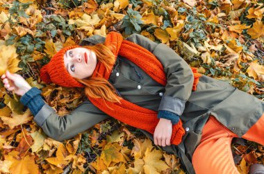 Kızıl saçlı, siyah gözlü ve sonbahar ormanında doğanın tadını çıkaran hayalperest kadın. Park yapraklarının üzerinde yatan kızın yakın plan portresi..