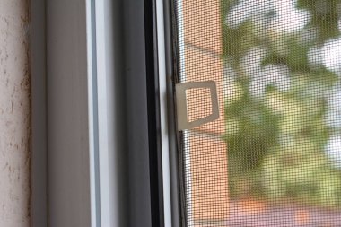 Plastik bir pencereye monte edilmiş sivrisinek ekranının yakın çekimi. Sivrisinek ve sineklerden korunmak için camlarında cibinlik var..  