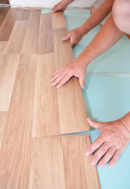 Laminate döşeme kurulumu. Erkekler plastik kaplamalı döşemeleri buhar mavisi bir zeminin üzerine kuruyorlar..