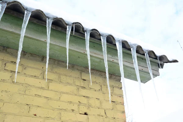 Ice icicles hanging from the roof without a roof gutter. Ice dams hang along the eave of the house.