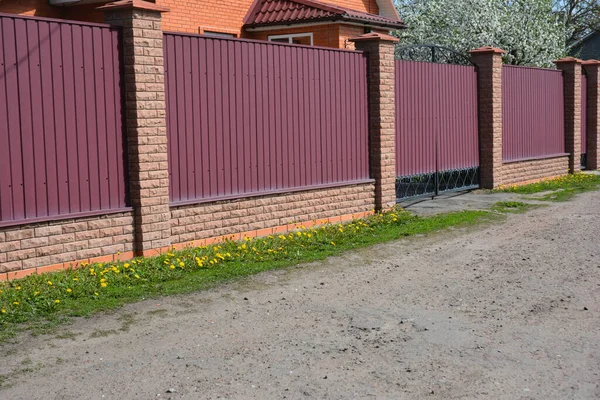砖墙砖墙砖房附近带有砖基和支撑柱子的金属红色栅栏和大门 — 图库照片