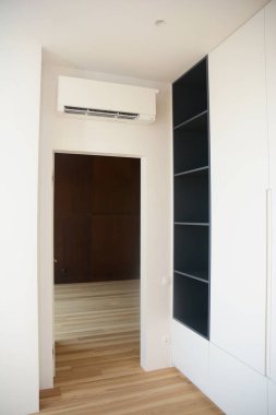 Kapının üstündeki duvara klima monte edilmiş bir oda, siyah panelleri ve ahşap döşemeleri olan beyaz bir gardırop. Duvara monte edilmiş bir klima ünitesi için iyi bir yer..