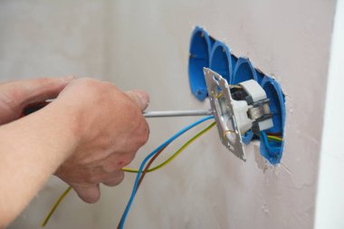 Yeni elektrik prizi kurulumu. Bir elektrikçi elektrik kablolarını elektrik kutusuna bağlayıp prizin kapağını vidalıyor. Elektrik prizi yerinde..