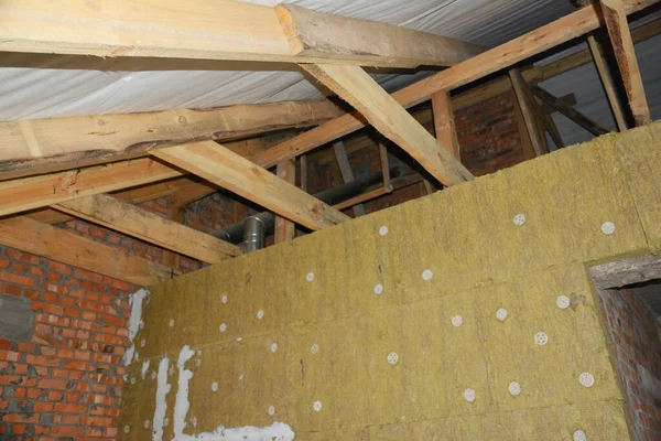 Roofing construction and wall insulation. A view from inside the house of unfinished attic construction with a wooden roof framing and a glass, mineral wool wall insulation.