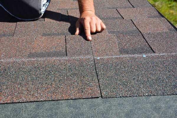Asphalt roof shingles installation. A roofer is nailing bitumen, asphalt roofing shingles properly along the nailing line. 