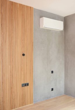 Modern oturma odası tasarımı: Ahşap paneller ve gri Venedik sıvası kombinasyonu, gri duvar kaplaması klima ve elektrik düğmeleri ve prizlerle bitiriliyor.