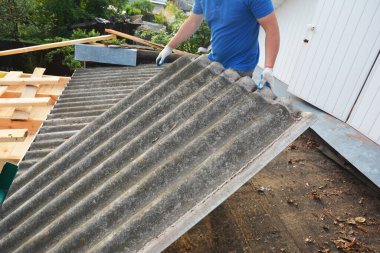 Old asbestos cement roof removal and replacement. A roofing contractor is removing old asbestos roofing sheets while roof renovation.  Roofing Construction.